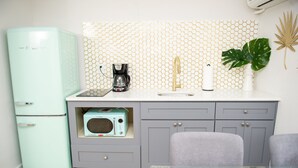 A compact kitchen with a vintage refrigerator, a microwave, a coffee maker, and a sink with a gold faucet. - Sunburst Inn The Beachside Suite - Room 5 (Indian Shores)