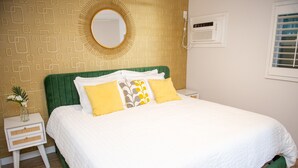 A neatly made bed with white and yellow bedding, a green upholstered headboard, and a small bedside table with a vase of flowers. - Sunburst Inn The Beachside Suite - Room 5 (Indian Shores)