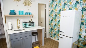 Cozinha compacta com geladeira branca, pia e bancada com louças azuis e cafeteira.