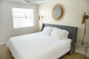 Een net opgemaakt bed met witte lakens, een ronde spiegel met gouden lijst en een moderne vloerlamp.