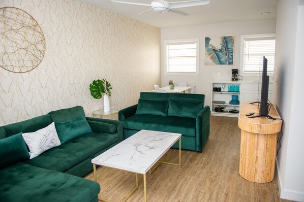 A living room with a green sofa, a white coffee table, and a wooden side table.