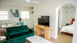 Een moderne woonkamer met een groene bank, een witte salontafel en een tv op een houten dressoir.