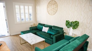 Een woonkamer met een groene bank, een witte salontafel en een grote plant.