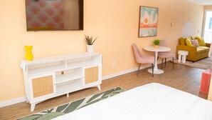 Ein modernes Zimmer mit einem Bett, einem weißen Konsolentisch, einem kleinen runden Tisch mit Stühlen, einem gelben Sofa und einem Gemälde an der Wand.
