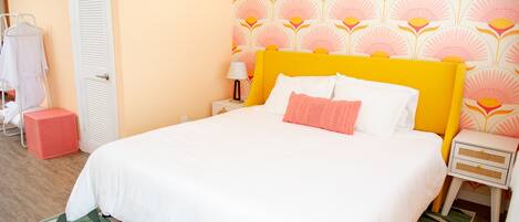 Een net opgemaakt bed met witte en roze beddengoed, een geel hoofdeinde en een behang met patroon.