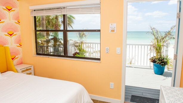 Ein Schlafzimmer mit großem Fenster und Blick auf den Strand und Palmen.