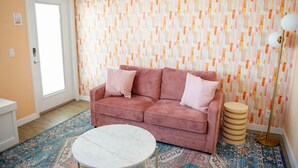 A living room with a pink sofa, a round white table, patterned rugs, and a wall with a geometric wallpaper design. - Sunburst Inn The Beachfront Suite - Room 11 (Indian Shores)