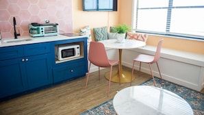 A kitchen with blue cabinets, a microwave, a toaster, and a window seat with two pink chairs. - Sunburst Inn The Beachfront Suite - Room 11 (Indian Shores)