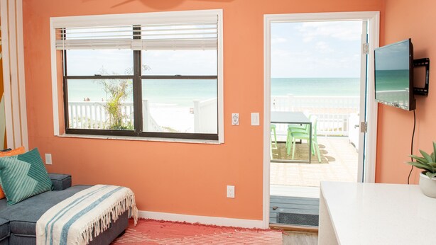 Une chambre avec une grande fenêtre donnant sur la plage, un ventilateur de plafond et un téléviseur fixé au mur.
