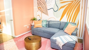 Un salon chaleureux avec un canapé bleu, une table basse ronde et une fresque murale aux couleurs vives.