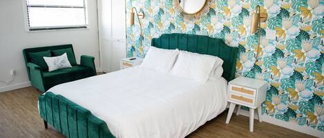 Een slaapkamer met een groot bed, een groene fauteuil, een nachtkastje en bloemenbehang.