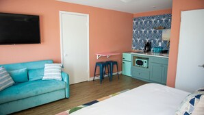 Een kamer met een smaragdgroene bank, een bed, een kitchenette met een magnetron en een plafondventilator.