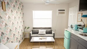 Ein gemütlicher, kompakter Wohnraum mit Sofa, Couchtisch, Küchenzeile und einem Fenster mit Jalousien.