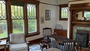 A cozy living room with a fireplace, a chandelier, and a view of greenery through large windows. - Historic 2 bedroom home in downtown Stevensville. Pet friendly! RV parking (Stevensville)