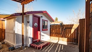 A small, single-story building with a red door and a small window, surrounded by a wooden fence and a dirt yard. - Mt Williamson Motel and Basecamp (Independence)