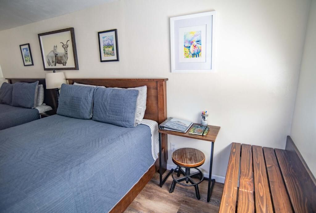 Un dormitorio con una cama grande, una mesita pequeña con un taburete y cuadros en la pared.