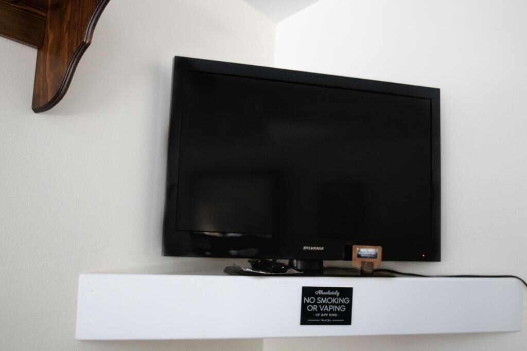 A flat-screen TV mounted on a white wall with a 'No Smoking or Vaping' sign below it.