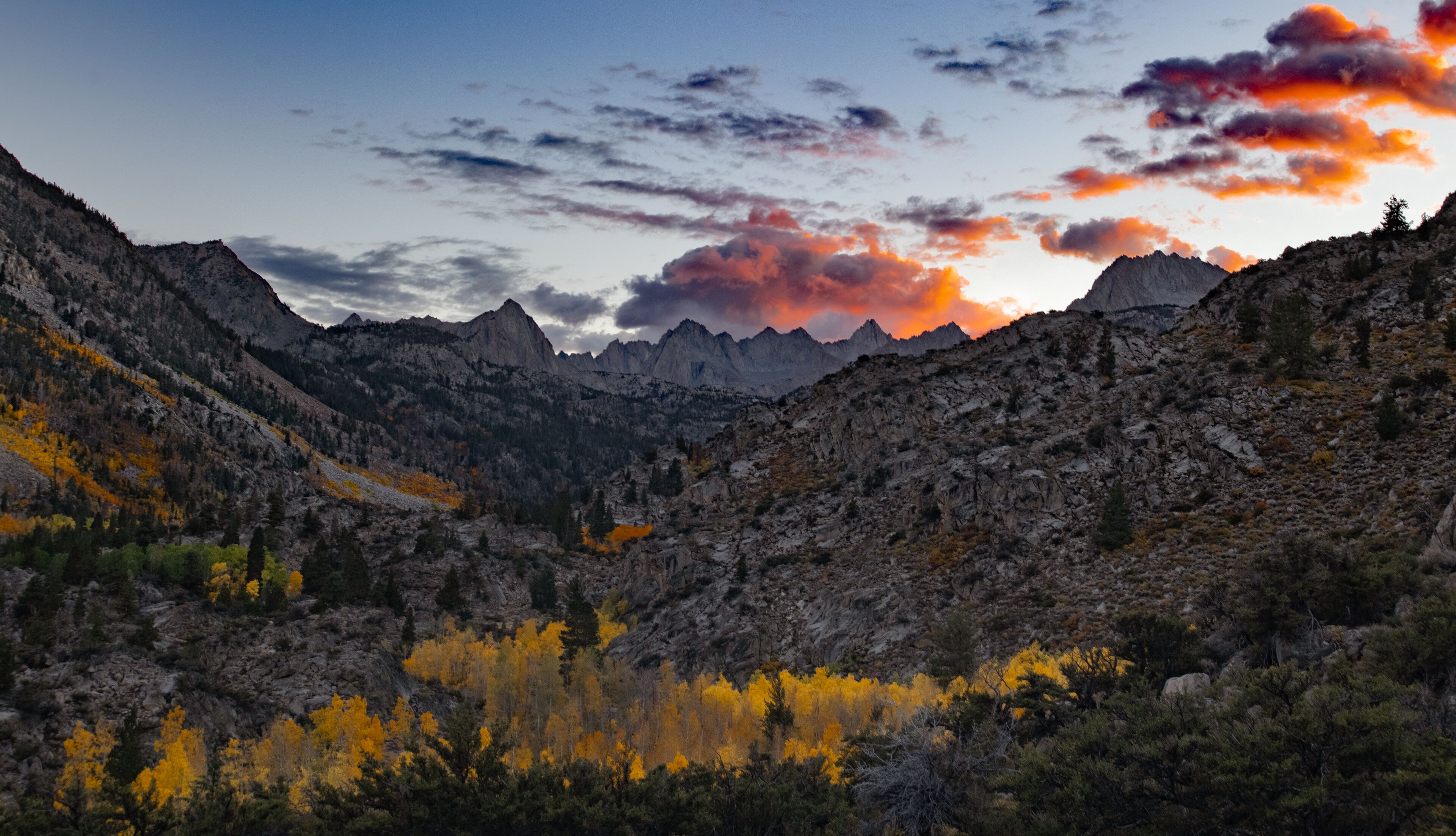 A mountainous landscape with autumn foliage and a sunset.