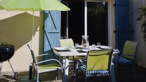 Un patio exterior con una mesa, sillas y una parrilla.