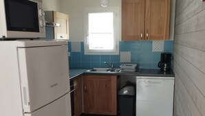 Una cocina compacta con armarios de madera, un refrigerador blanco, un microondas, un lavamanos y una ventana.