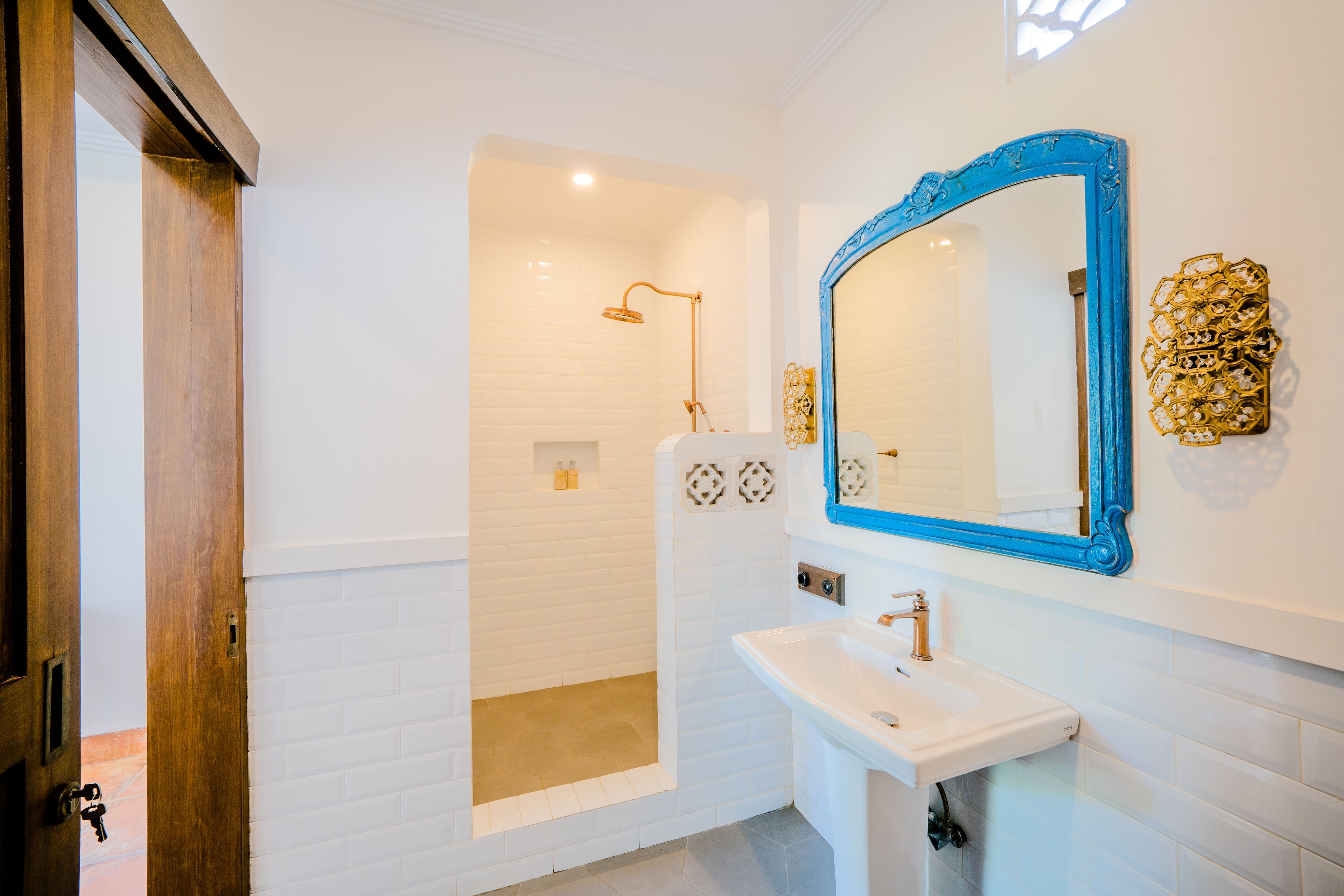 Une salle de bain moderne avec une douche carrelée de carreaux blancs, un lavabo doté d’un robinet doré et un miroir à cadre bleu.