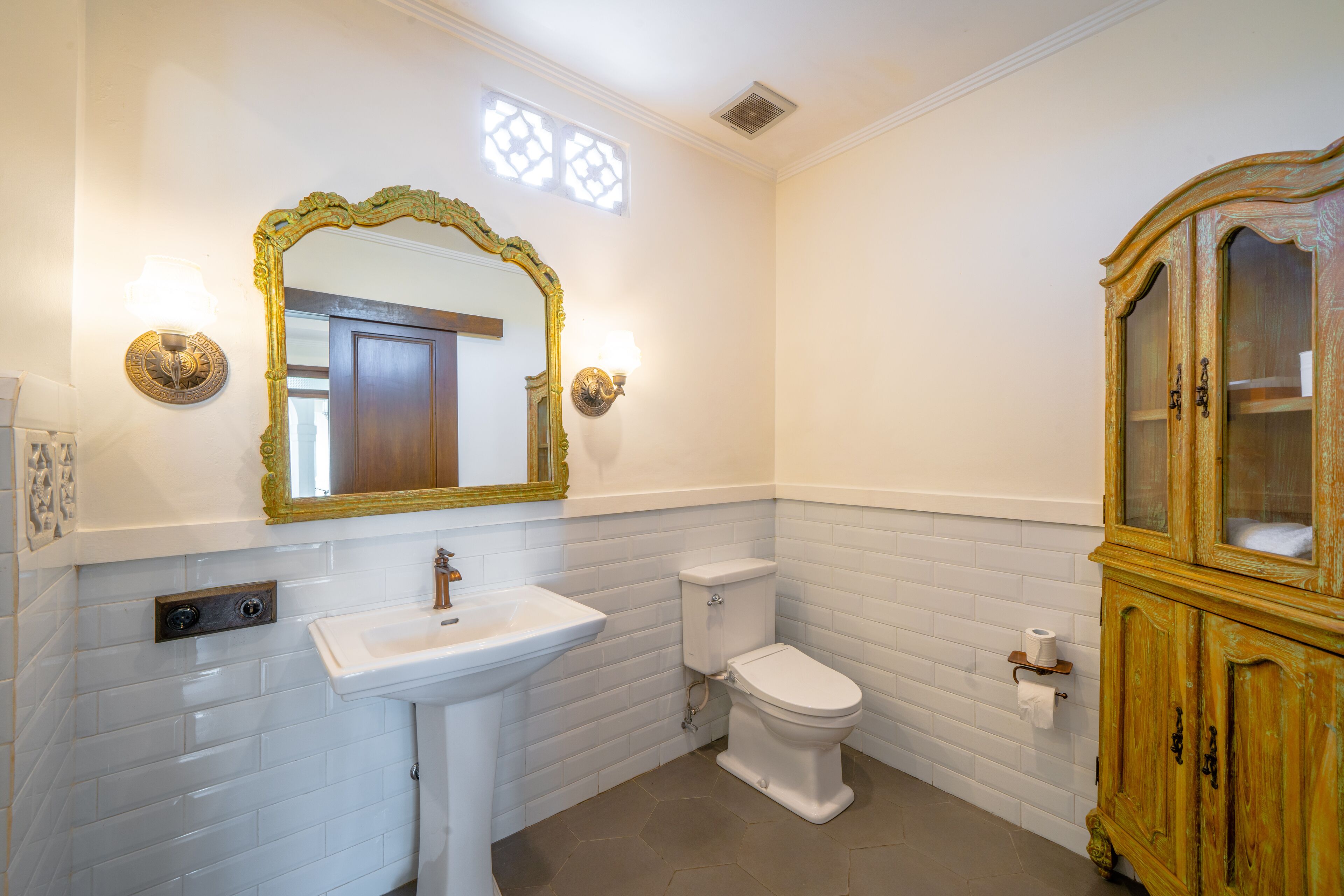 Un baño con lavamanos blanco, inodoro y un armario de madera.