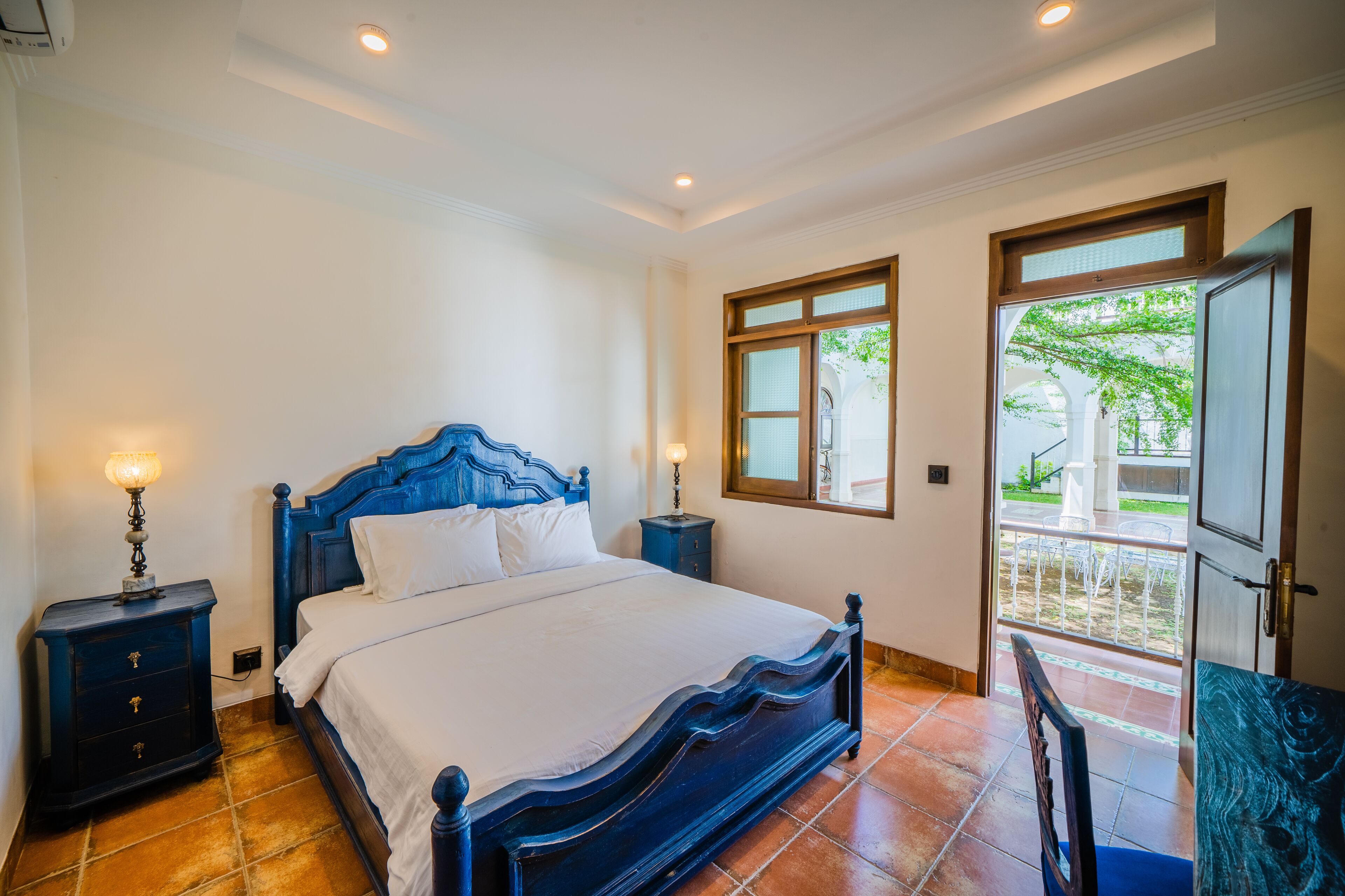 A bedroom with a large bed, two bedside tables, a nightstand, and a door leading to a balcony.