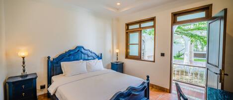 A bedroom with a large bed, two bedside tables, a nightstand, and a door leading to a balcony.