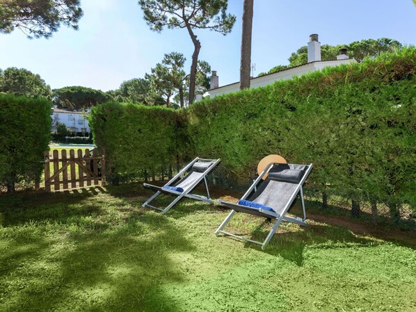A garden with two sun loungers, a wooden fence, and a hedge.