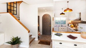 Una cocina moderna con armarios blancos, una escalera de madera y vistas al exterior a través de una ventana.