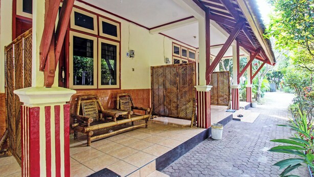A covered outdoor area with a wooden bench, a tiled floor, and a view of greenery. - Hotel O Losmen Tjabe Merah Near Alfamart Bintaro (Purwokerto)