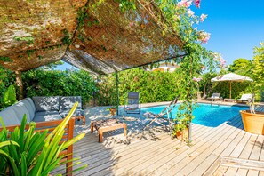 A wooden deck with a pool, lounge chairs, and a covered seating area.