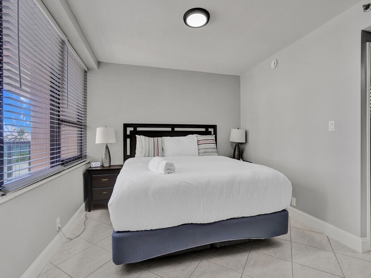 A bedroom with a bed, nightstands, a window with blinds, and a ceiling light.