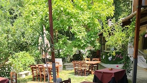 An outdoor patio with tables and chairs, covered by a metal roof, surrounded by greenery. - MoMa RoofGarden (San Polo Matese)