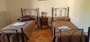 Une chambre avec deux lits jumeaux, chacun recouvert d’une courtepointe marron matelassée et agrémenté d’oreillers. Une table de chevet en bois avec une lampe se trouve entre les deux lits.