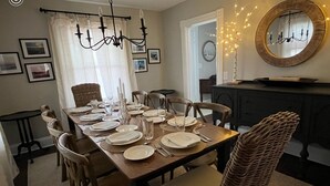 Une salle à manger avec une table en bois dressée pour quatre personnes, entourée de chaises en osier. Un lustre est suspendu au-dessus de la table et un miroir orne le mur.