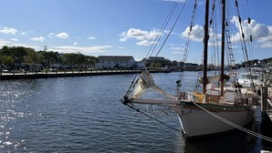 Un voilier est amarré dans une marina, avec des bâtiments et des arbres en arrière-plan.