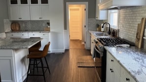 Une cuisine avec des meubles blancs, un plan de travail en granit, un plancher en bois et un tabouret de bar.