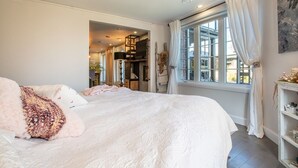 Un dormitorio con una cama grande, una ventana con cortinas, una estantería y un cuadro en la pared.