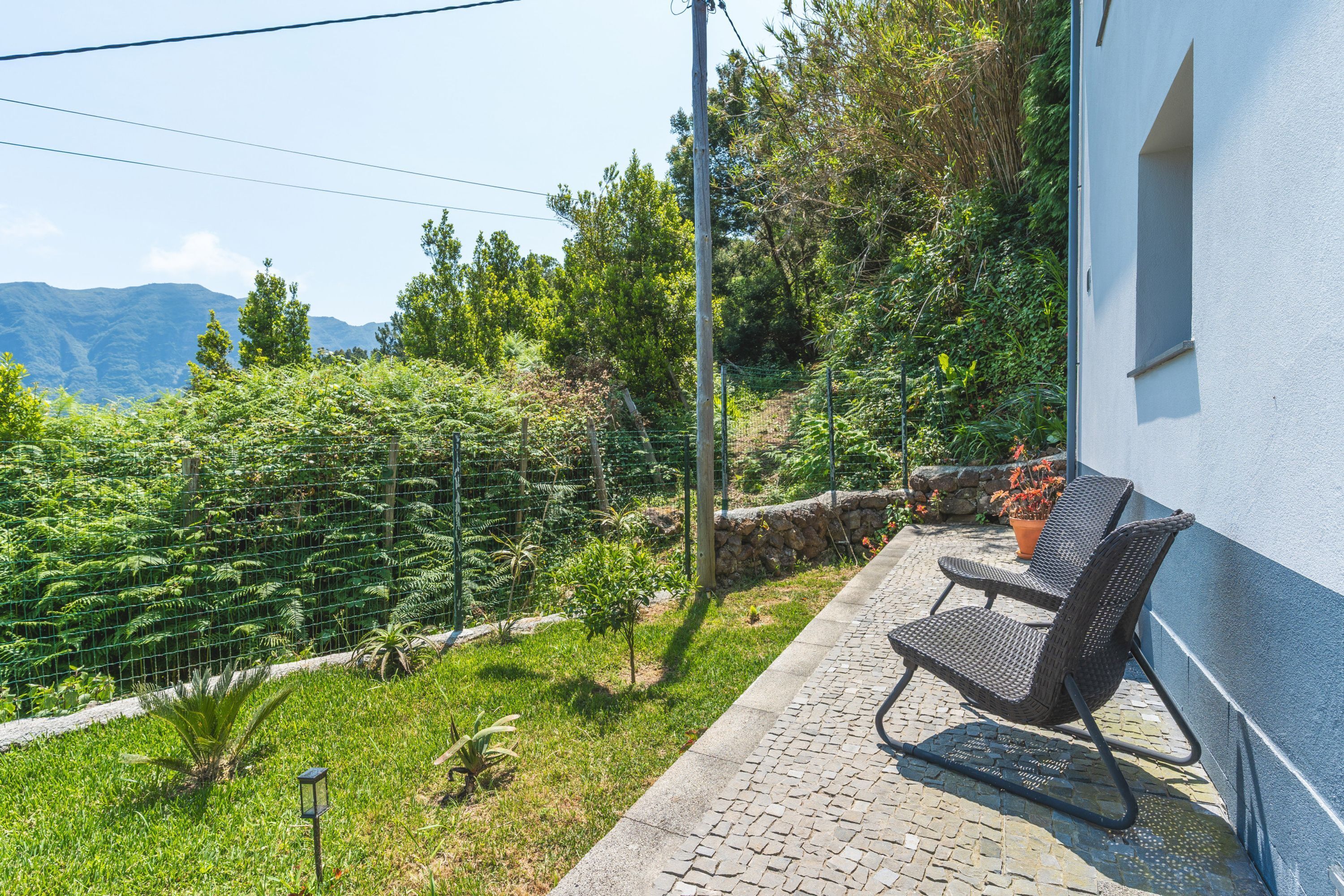 A patio with a chair and table, surrounded by greenery and a mountain view.
