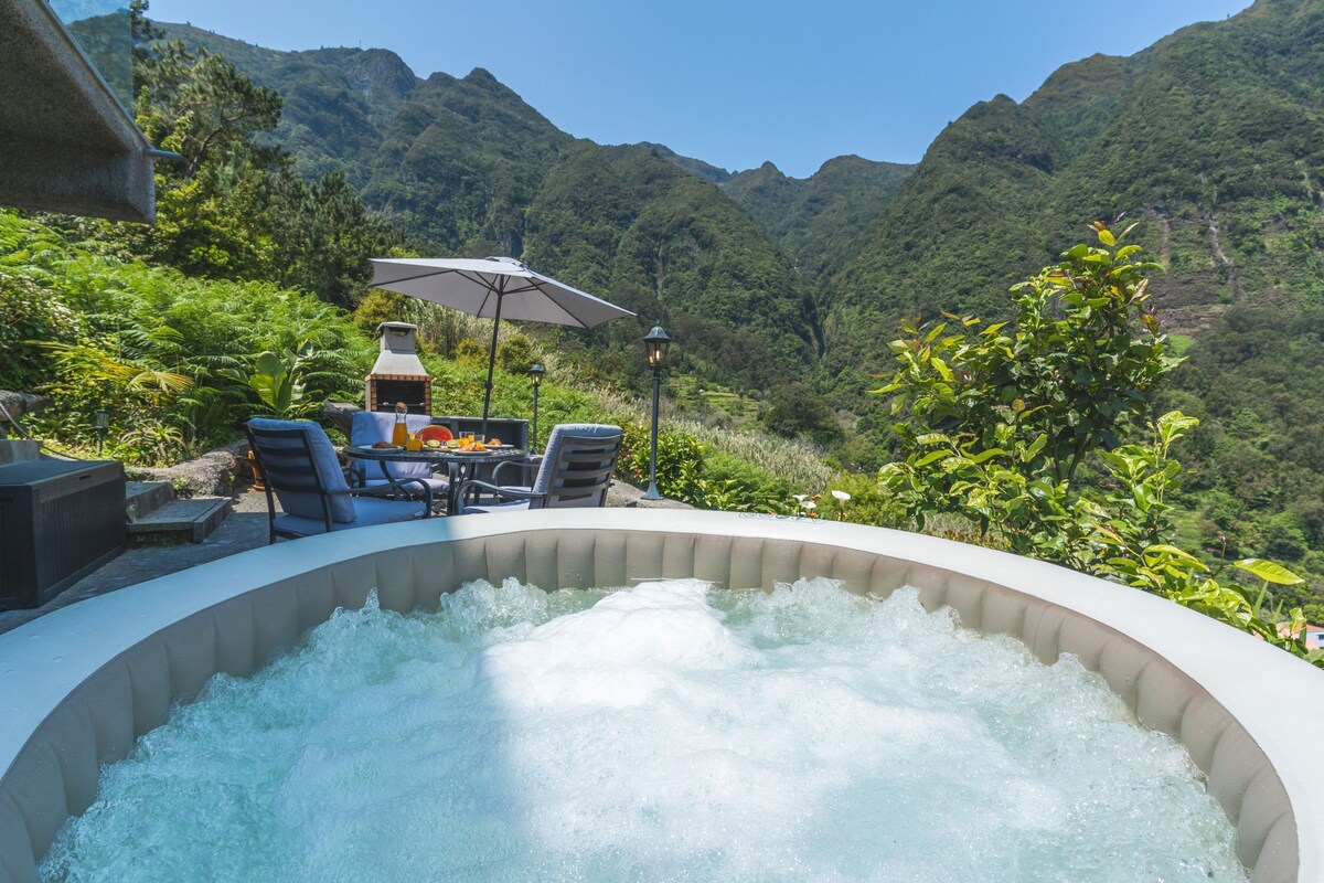 A hot tub surrounded by outdoor furniture and a barbecue grill, set against a mountainous backdrop.