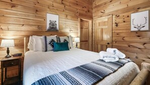 Een kamer met houten lambrisering, een bed, een nachtkastje, een lamp en twee ingekaderde foto's aan de muur.