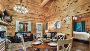 Een gezellig interieur van een chalet met een eethoek, een woonkamer met een bank en een televisie, en een apart slaapgedeelte met een bed.