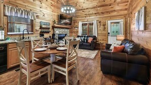 Een gezellig interieur van een chalet met een eethoek, een open haard, een woonkamer met een bank en een koffiebar.