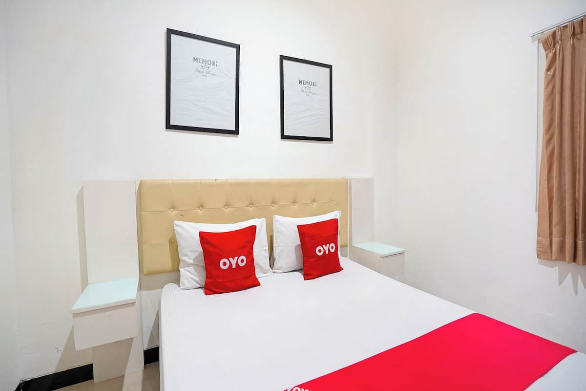 A hotel room with a bed, two framed pictures on the wall, a nightstand, and a window with curtains.