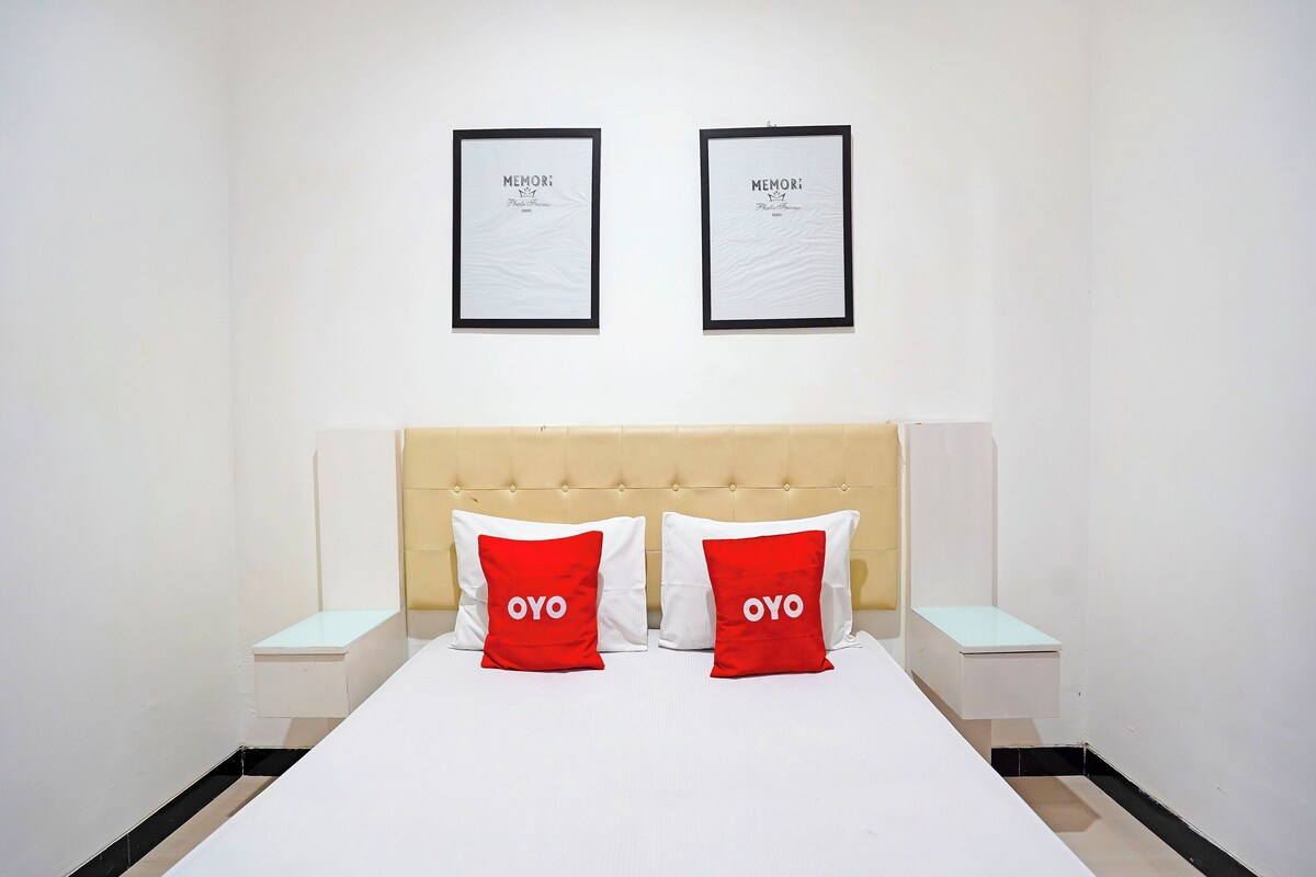 A hotel room with a bed, two framed pictures on the wall, and two red pillows with the word 'OYO' on them.