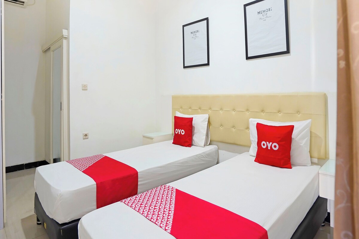 A hotel room with two beds, each with a red and white bedspread and matching pillows. There are two framed certificates on the wall.