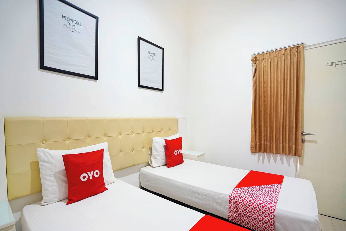 A hotel room with two beds, a beige headboard, a brown curtain, and two framed pictures on the wall.