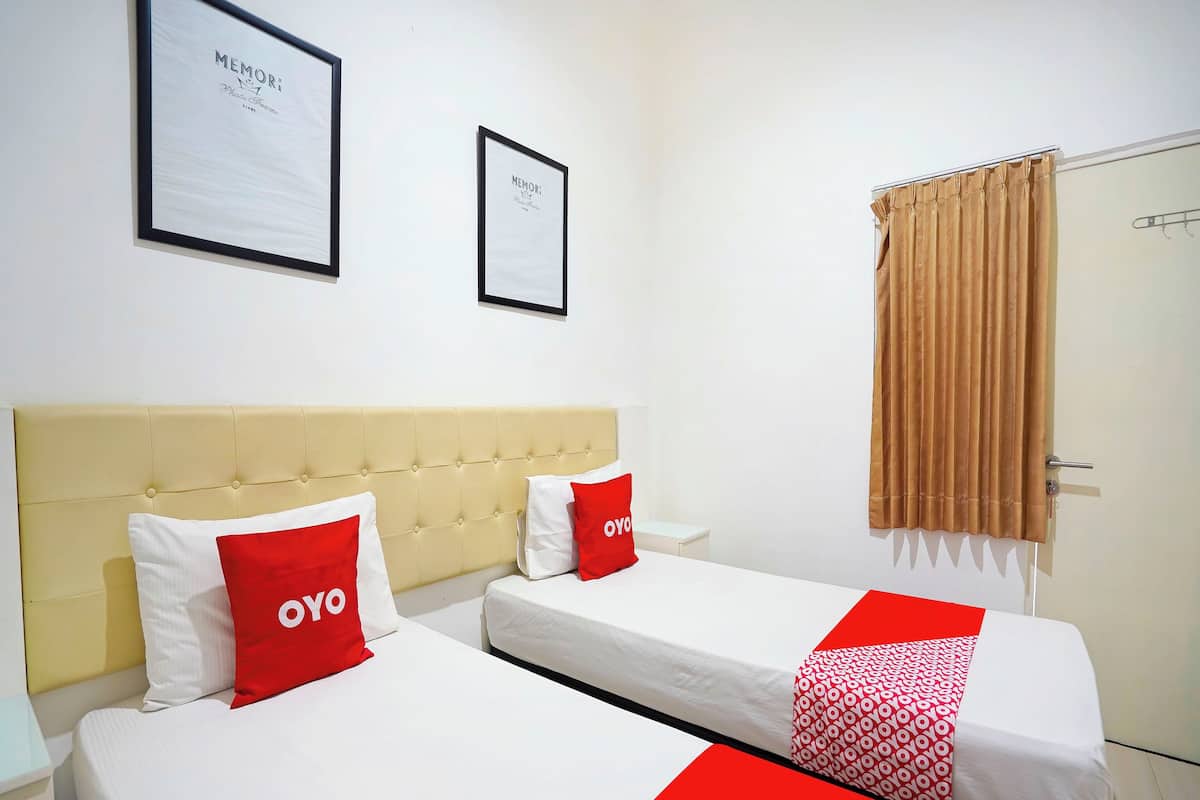 A hotel room with two beds, a beige headboard, a brown curtain, and two framed pictures on the wall.