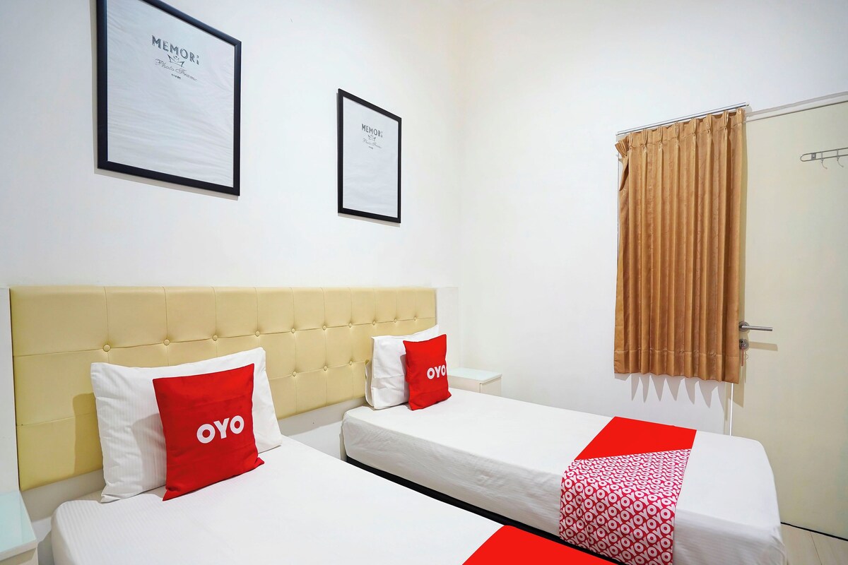 A hotel room with two beds, a beige headboard, a brown curtain, and two framed pictures on the wall.
